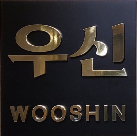 검은 바탕에 금색으로 ‘우신 WOOSHIN’이라고 쓴 사무소 현판